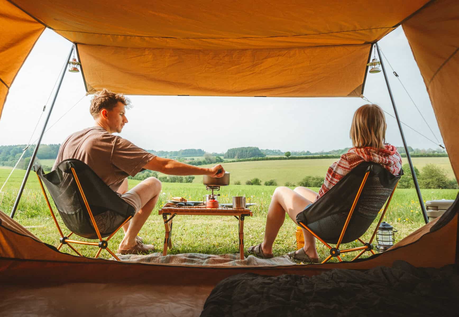 Entspanntes camping, junge leute beim zelten in der natur, grillen und draußen sitzen, weitblick in grüne wiesen und bäume, outdoor-urlaub, abenteuer und freude in der Natur, campingausrüstung, gelände und freiheit, freizeit und entspannung, Familien- und Freundeaktivitäten.