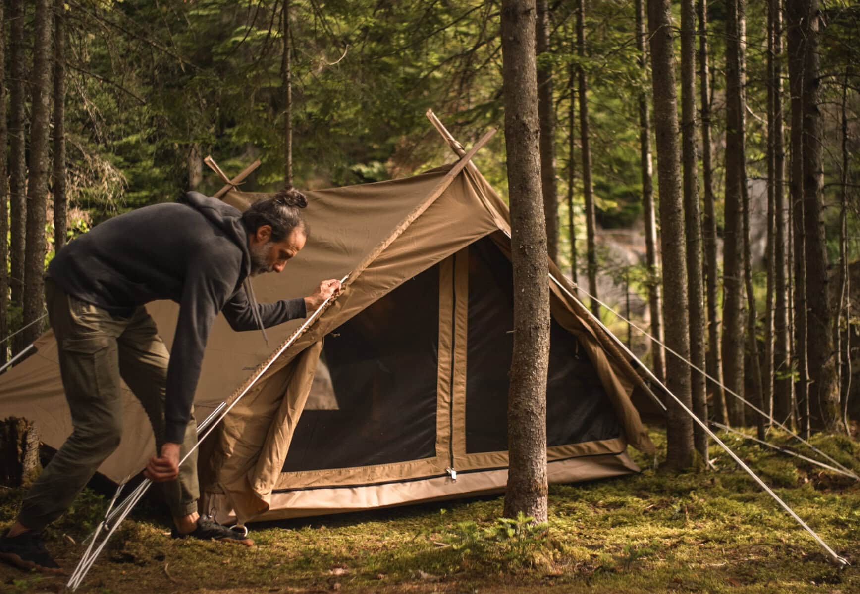 Robuster Mann beim Aufbau eines Zelt im Wald, Camping, Natur, Outdoor-Abenteuer, nachhaltiger Urlaub.