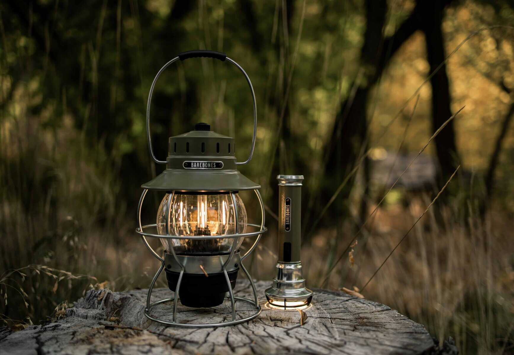 Leuchtende Campinglaterne und Rauchrohr auf Baumstumpf in Waldkulisse bei Dämmerung, outdoor, langlebige Elektrolaterne, ideal für Camping und Wanderungen, robustes und stilvolles Design.