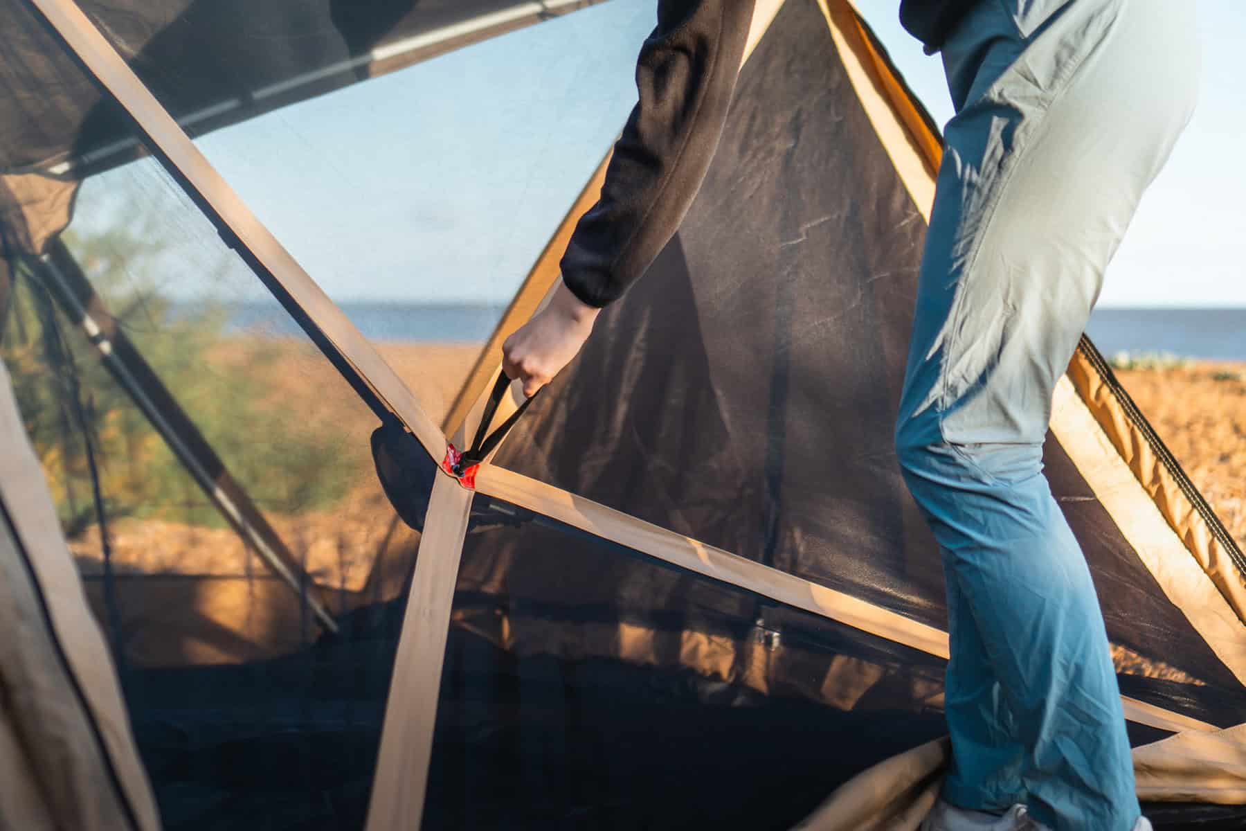 Robuster Aufbau eines Campingzelts, das von einer Person an einem sonnigen Strand aufgestellt wird, ideal für Outdoor-Abenteuer und Campingurlaub am Meer.