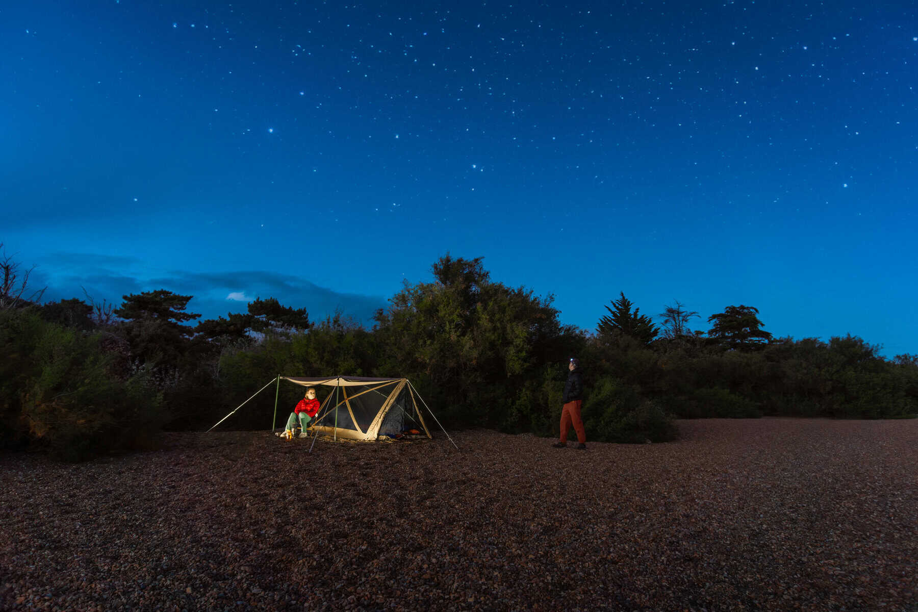 Sternenhimmel über Zeltplatz bei Nacht, Camping unter freiem Himmel, Naturlandschaft mit Sternschnuppen, Outdoor Abenteuer, ideales Bild für Camping und Natur.