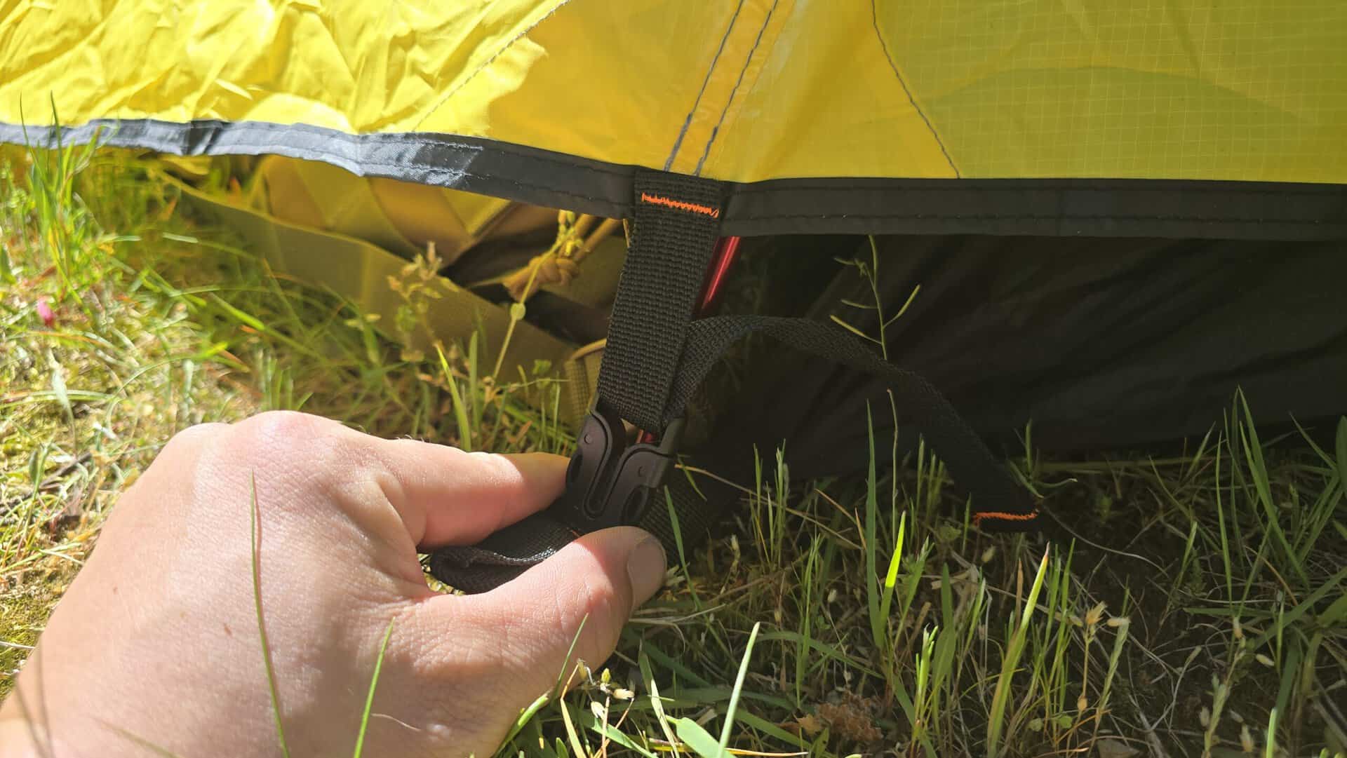 Helles gelbes Zelt auf grünem Gras, mit Hand, die den Zeltverschluss hält, ideal für Trekking und Camping, leicht und tragbar, perfekt für Outdoor-Abenteuer, nur 5 €/Tag + 50 € Kaution.
